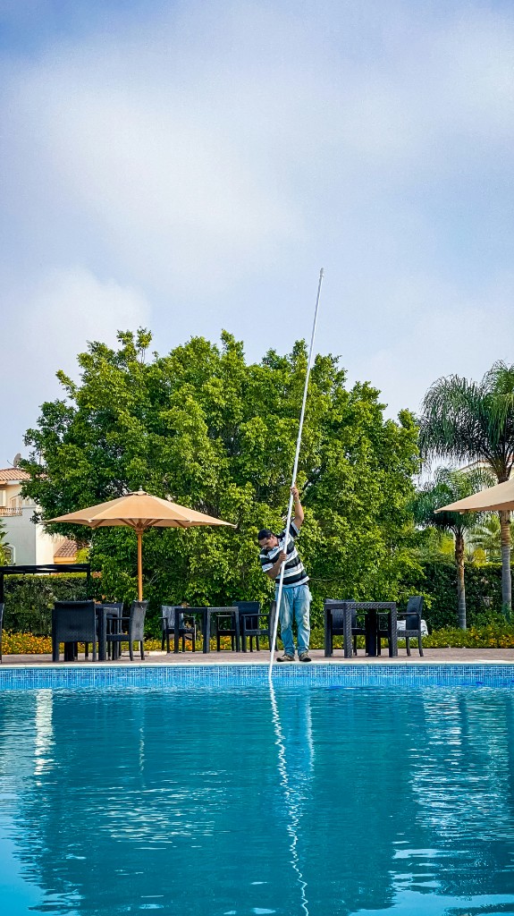 Pool technician skimming a residential swimming pool with a telescopic pole